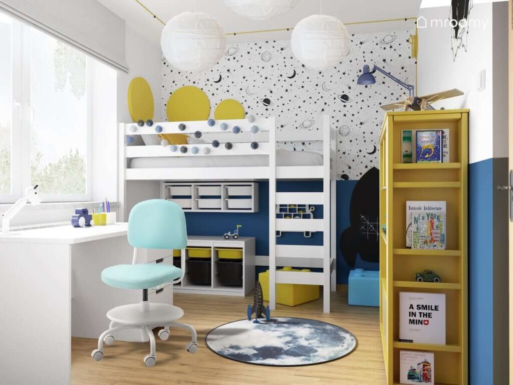Kolorowy pokój dla chłopca z łóżkiem na antresoli oraz pojemnikami na zabawki pod antresolą a także białym biurkiem i tapetą w gwiazdy planety i księżyce z księżycowym dywanem