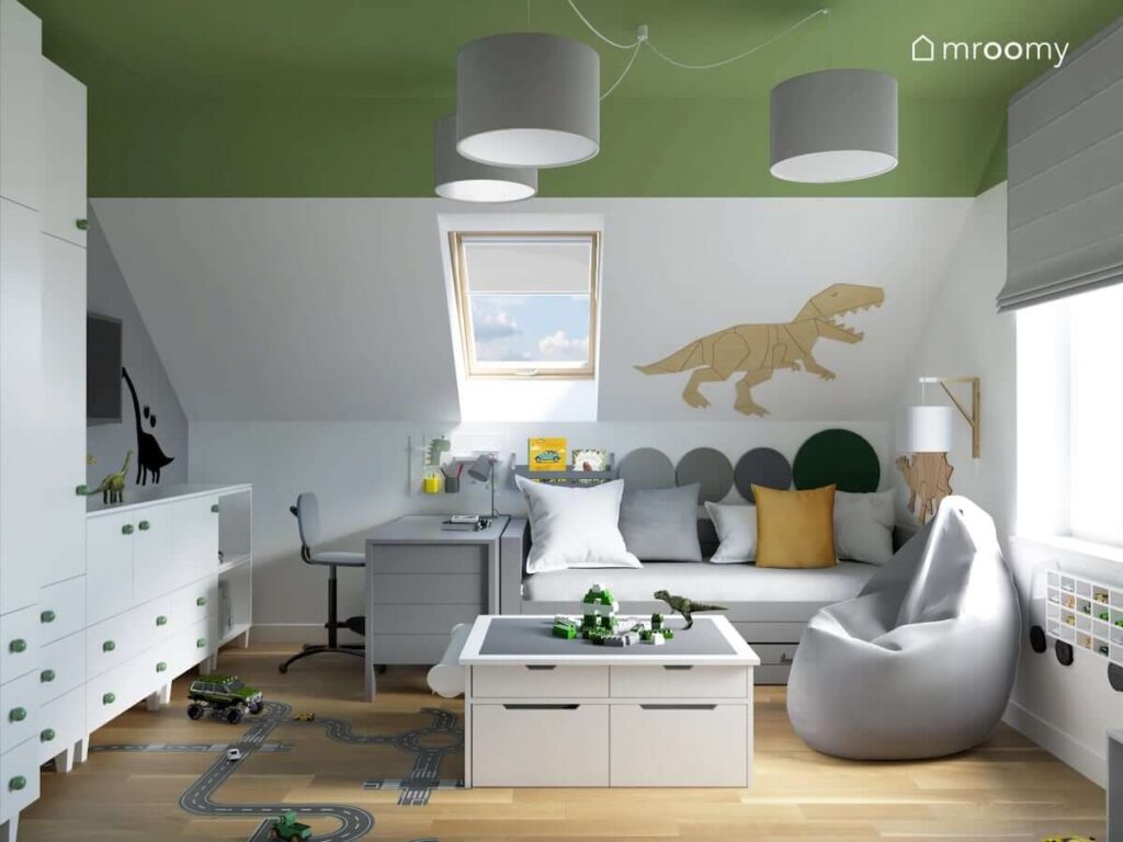 Poddaszowy pokój dla chłopca z szarymi i białymi meblami zielonym sufitem oraz dinozaurami ze sklejki na ścianach