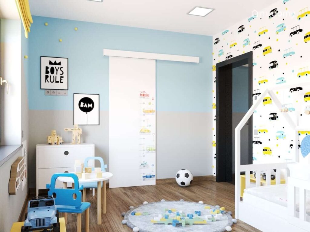 Pokój dla dwóch chłopców z niebiesko szarymi ścianami i tapetą w kolorowe samochody a także miarką wzrostu w samochody i ozdobnymi plakatami z napisami na ścianie