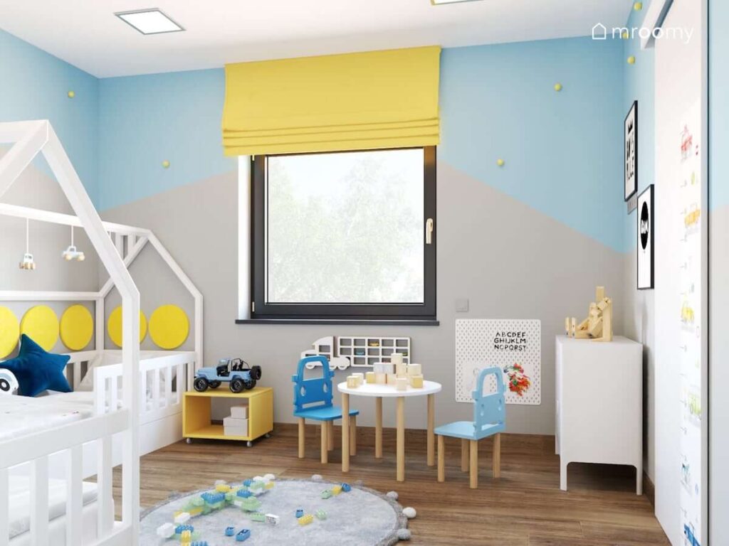 Niebiesko szary pokój dla dwóch chłopców z żółtymi akcentami białymi meblami a także stolikiem dziecięcym i krzesełkami z oparciami w kształcie aut