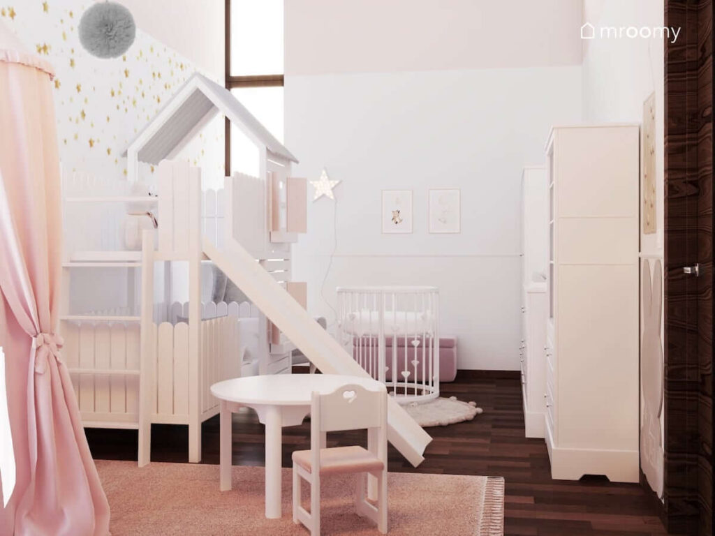 Jasny pokój dla dziewczynki niemowlaka z łóżkiem z antresolą i zjeżdżalnią a także stolikiem z krzesełkiem oraz okrągłym łóżeczkiem rosnącym i ozdobnymi plakatami na ścianie