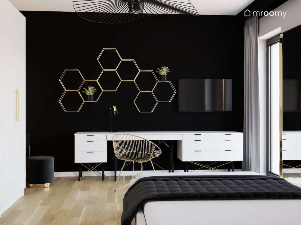 Czarno biało szary pokój dla nastolatki w stylu glamour z białym biurkiem i kontenerami oraz złotą półką ścienną w kształcie heksagonów na tle czarnej ściany