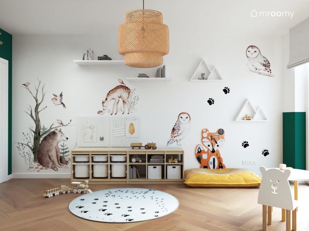 Ściana ozdobiona naklejkami w kształcie leśnych zwierząt a także półkami i naklejkami w kształcie śladów łapek a na suficie bambusowa lampa w pokoju dla chłopca
