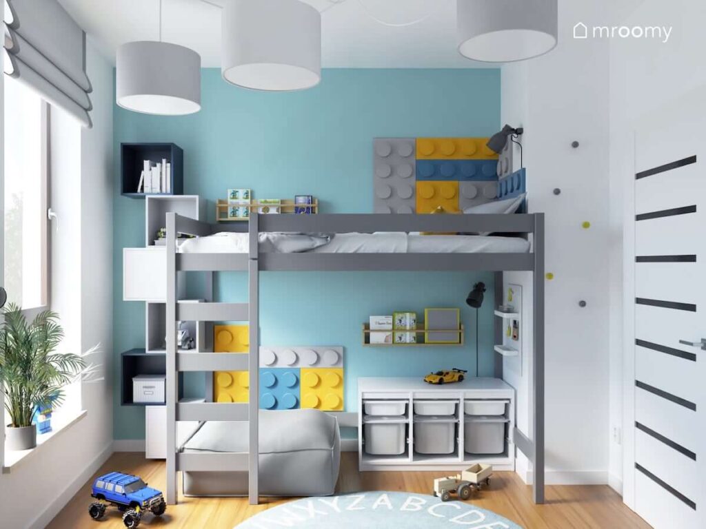 Szare łóżko na antresoli uzupełnione kolorowymi panelami ściennymi w kształcie klocków z miejscem do czytania oraz zabawy pod spodem a obok granatowe i białe szafki ścienne w biało niebieskim pokoju dla chłopca
