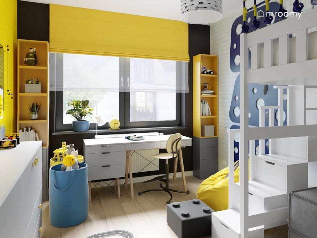 Żółto czarna strefa nauki w pokoju dla chłopca z dwoma wysokimi regałami oraz biurkiem a także koszami na zabawki w kolorze niebieskim
