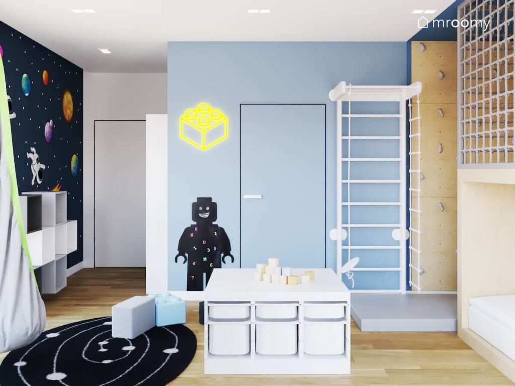 Biało niebieski pokój dla chłopca z drabiną gimnastyczną ścianką wspinaczkową oraz regałami z pojemnikami na zabawki i kosmicznym dywanem oraz tapetą i naklejkami na ścianie