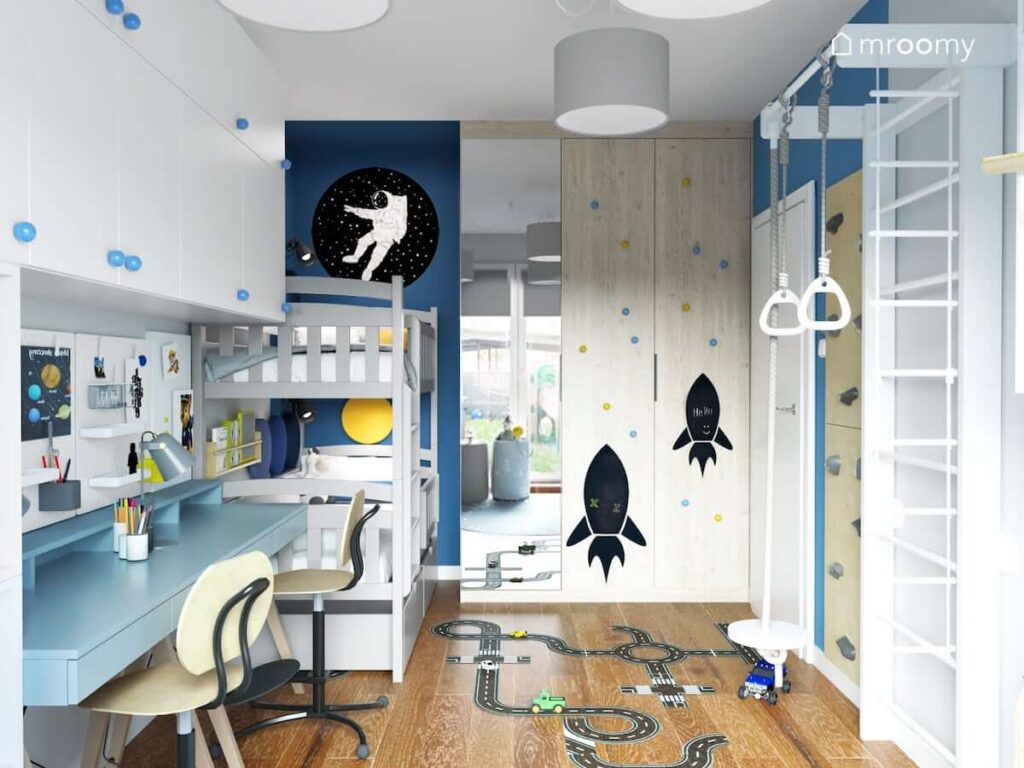 Biało niebieski pokój dla dwóch chłopców z białymi szafkami łóżkiem piętrowym i drewnianą szafą z lustrzanym frontem i kredowymi naklejkami w kształcie rakiet