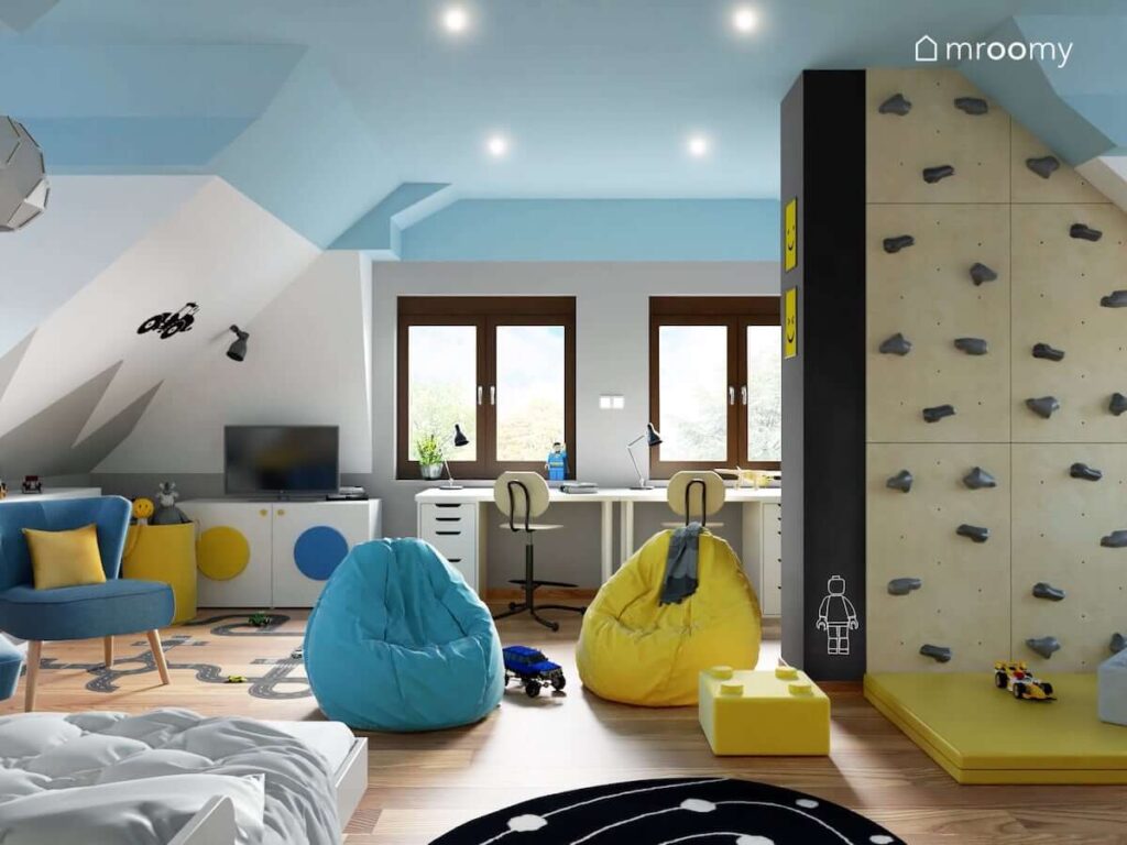 Biało niebieski pokój dla dwóch chłopców z białymi meblami oraz żółtymi i niebieskimi dodatkami a także ścianką wspinaczkową i ścianą pomalowaną farbą tablicową