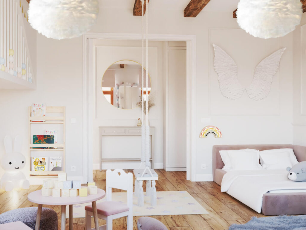 Biały pokój dla małej dziewczynki z szarą konsolą z okrągłym lustrem oraz z niskim pudrowo różowym łóżkiem nad którym wisi ozdoba w kształcie skrzydeł oraz lampka nocna w kształcie tęczy