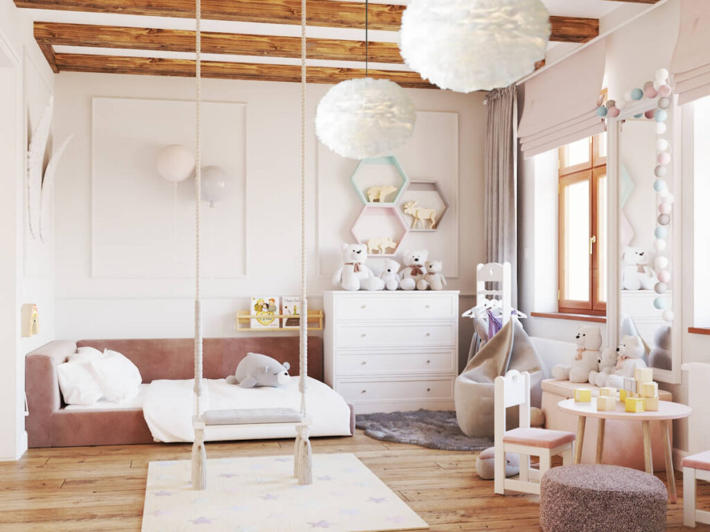 Jasny przestronny pokój dla dziewczynki z niskim pudrowo różowym łóżkiem huśtawką białymi meblami półką w kształcie heksagonów a także z dekoracyjnymi kinkietami w kształcie balonów i lampami sufitowymi z piór