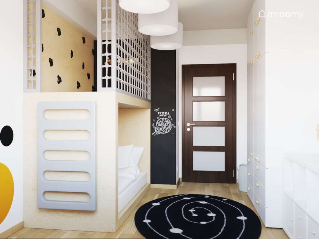 Antresola ze ścianką wspinaczkową a także z miejscem do spania pod spodem oraz czarno biały dywan i ściana pomalowana farbą tablicową w pokoju dla chłopca