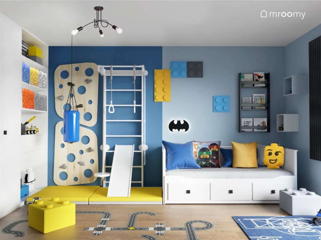 Biało niebieski pokój dla chłopca z białym łóżkiem drabinką gimnastyczną ścianką wspinaczkową i żółtymi materacami a także ze ścianą ozdobioną miękkimi panelami ściennymi w kształcie klocków