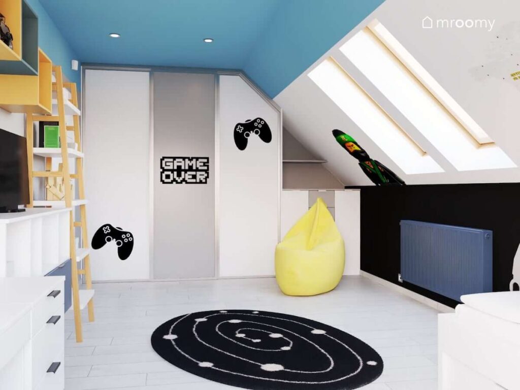 Biało niebieski poddaszowy pokój dla fana gier video z tematycznymi naklejkami na ścianach oraz białymi meblami z żółtymi i drewnianymi akcentami