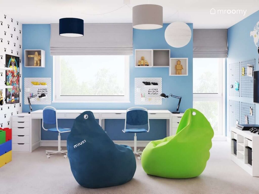 Strefa nauki w biało niebieskiej bawialni dwóch chłopców z dwoma biurkami organizerami i szafkami ściennymi a także dwie wygodne pufy sako