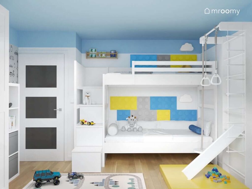 Białe łóżko piętrowe uzupełnione kolorowymi panelami ściennymi w kształcie klocków oraz drewnianą półką na książki i lampkami w kształcie chmurek w pokoju dla dwóch chłopców