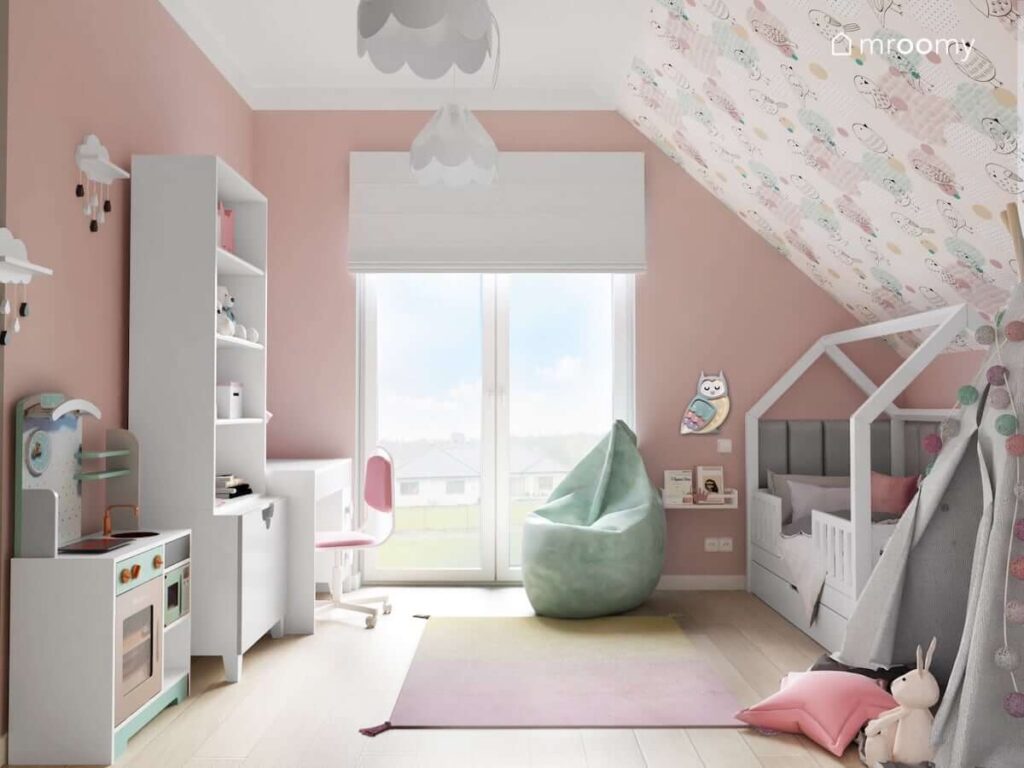 Różowy pokój dla dziewczynki z białymi meblami oraz szarymi dodatkami a także pastelową tapetą w ptaszki zdobiącą skos