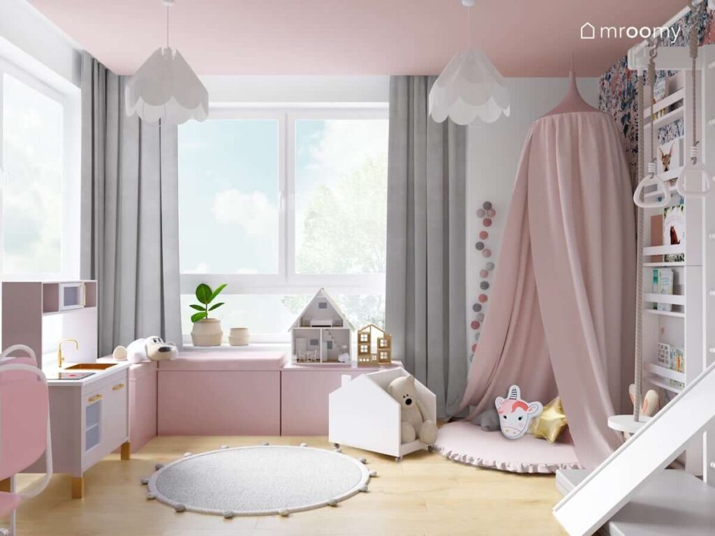 Biało różowa bawialnia dla dzieci z różowymi oraz szarymi dodatkami w postaci zasłon baldachimu dywanu i girlandy cotton balls
