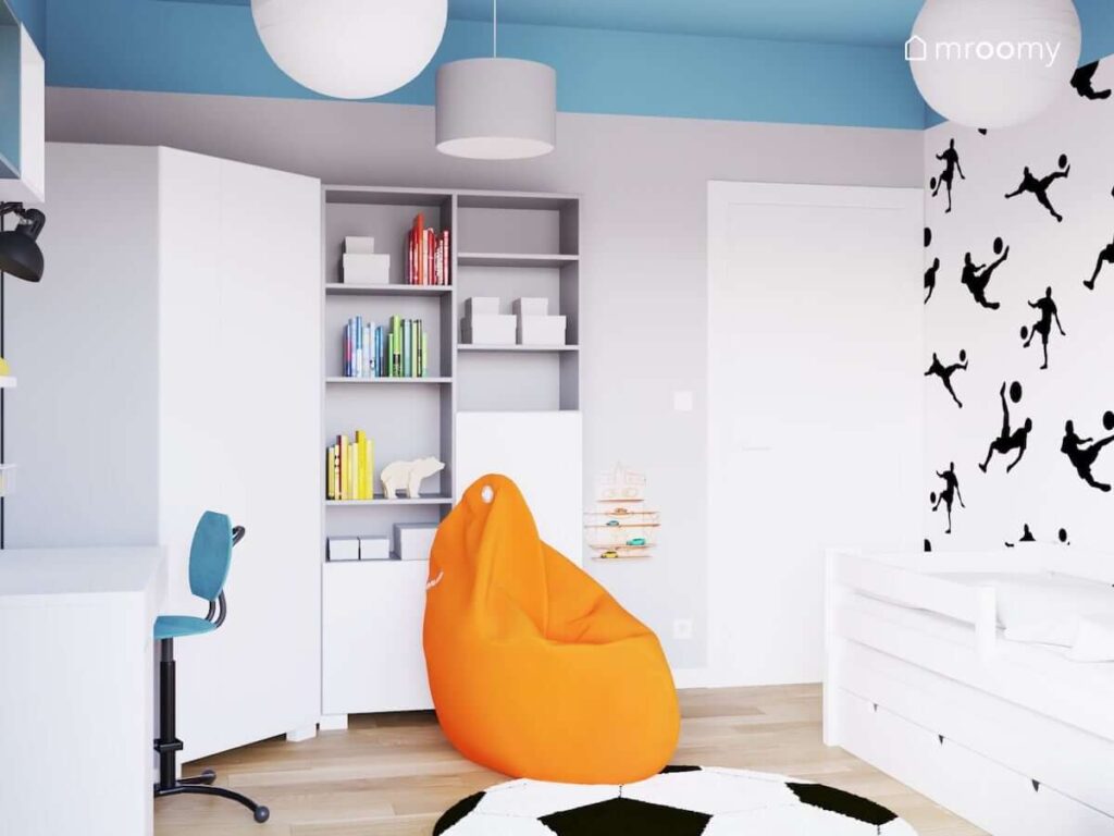 Biała szafa narożna wysokie regały oraz pomarańczowa pufa sako w pokoju dla chłopca fana piłki nożnej
