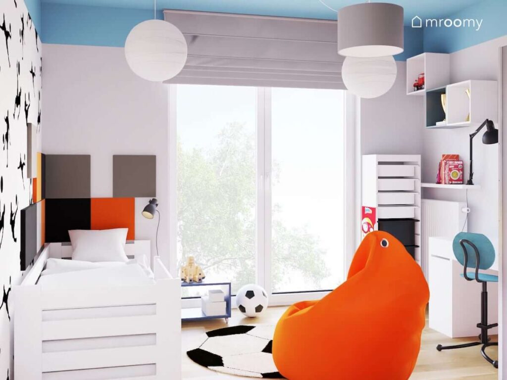 Białe łóżko uzupełnione szarymi czarnymi i pomarańczowymi panelami ściennymi a także białe meble i szare dodatki w pokoju dla chłopca