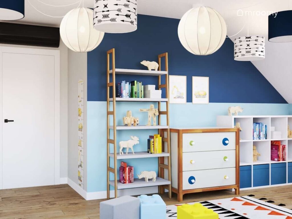Biało niebieski pokój dla chłopca z biało drewnianymi meblami rozłożystą lampą sufitową z kilkoma abażurami oraz z dodatkami z motywami budowy
