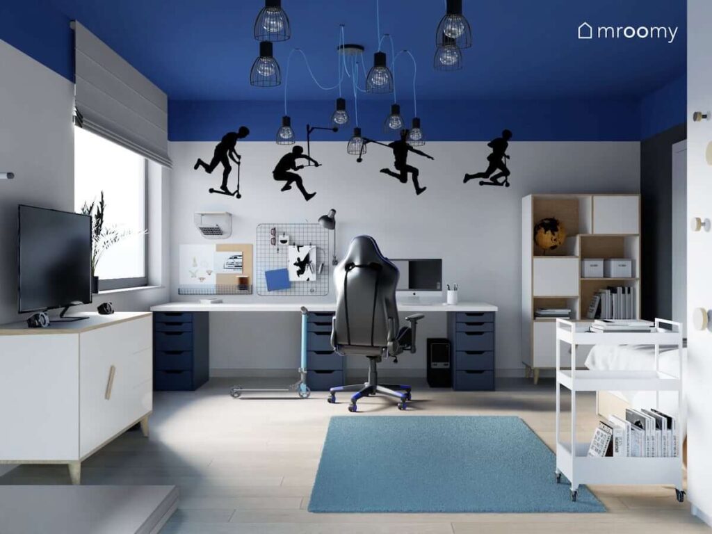 Niebiesko szary pokój dla miłośnika jazdy na hulajnodze z dużym biurkiem z organizerami biało drewniamnymi meblami naklejkami ściennymi i rozłożystymi lampami sufitowymi