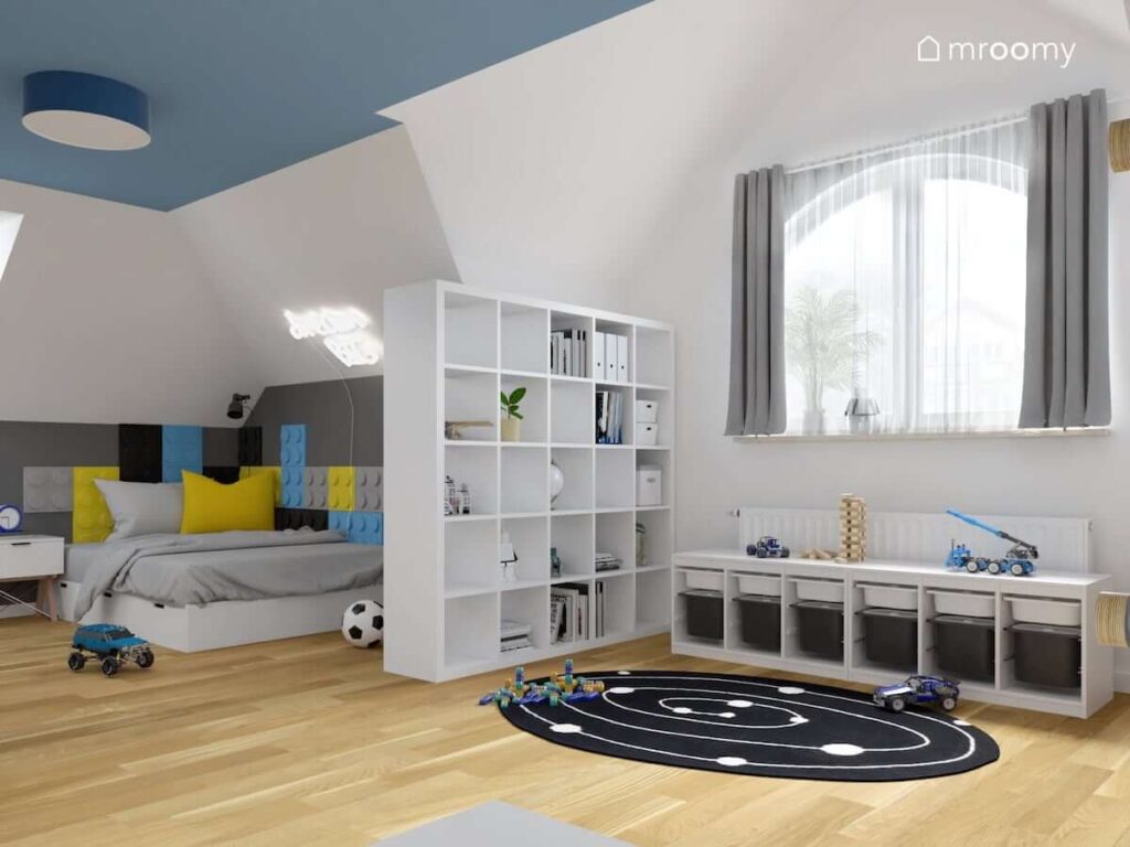 Jasny pokój dla chłopca z niebieskim sufitem oraz białymi meblami i łóżkiem uzupełnionym panelami ściennymi w kształcie klocków