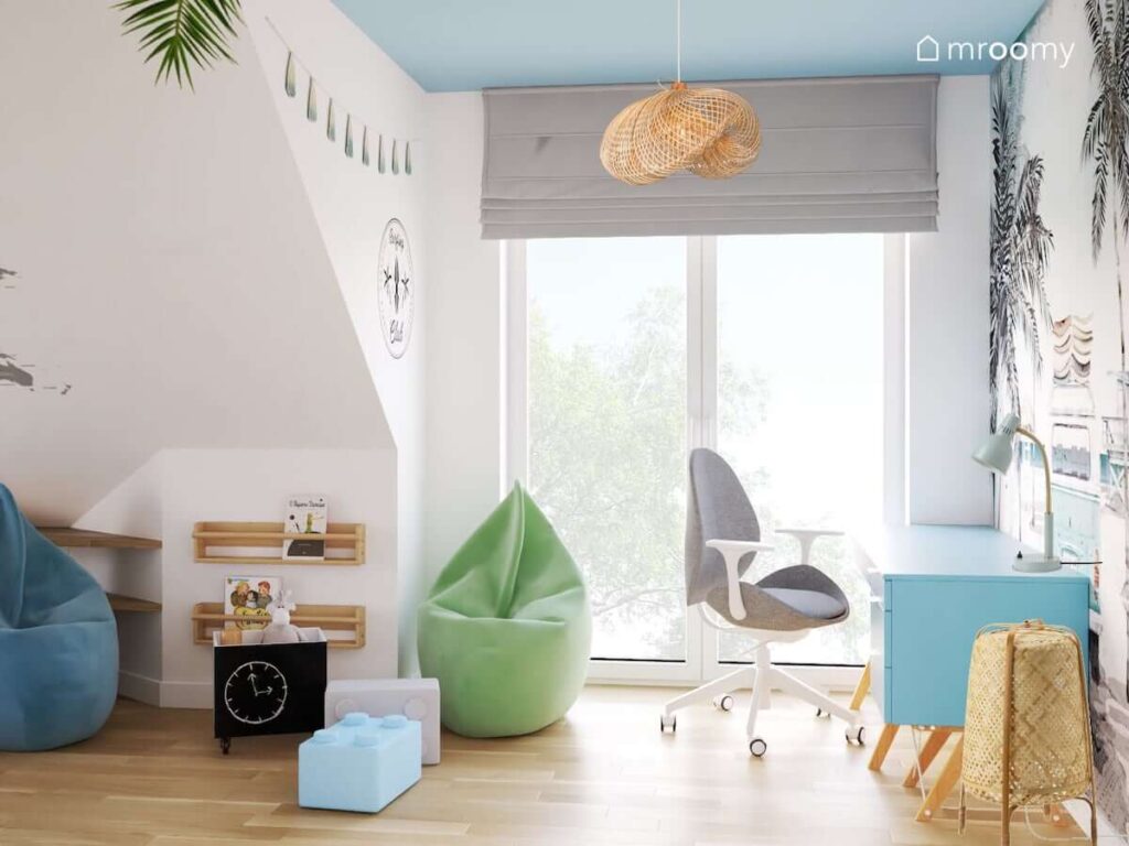 Jasny pokój dla chłopca z białymi ścianami i niebieskim sufitem oraz zieloną pufą sako drewnianymi szafkami ściennymi czarną skrzynką na zabawki i wiklinowym kloszem do lampy sufitowej