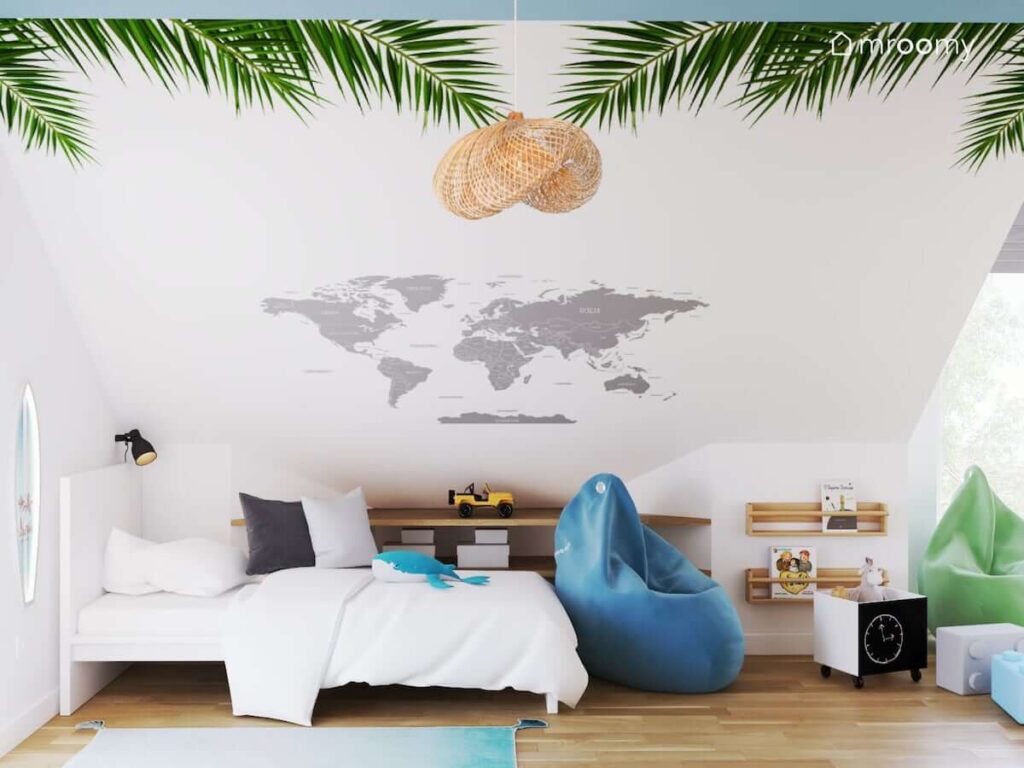 Strefa spania w pokoju dla chłopca z białym łóżkiem i lampką nocną w kształcie deski surfingowej oraz skosem ozdobionym mapą świata i naklejkami w kształcie liści