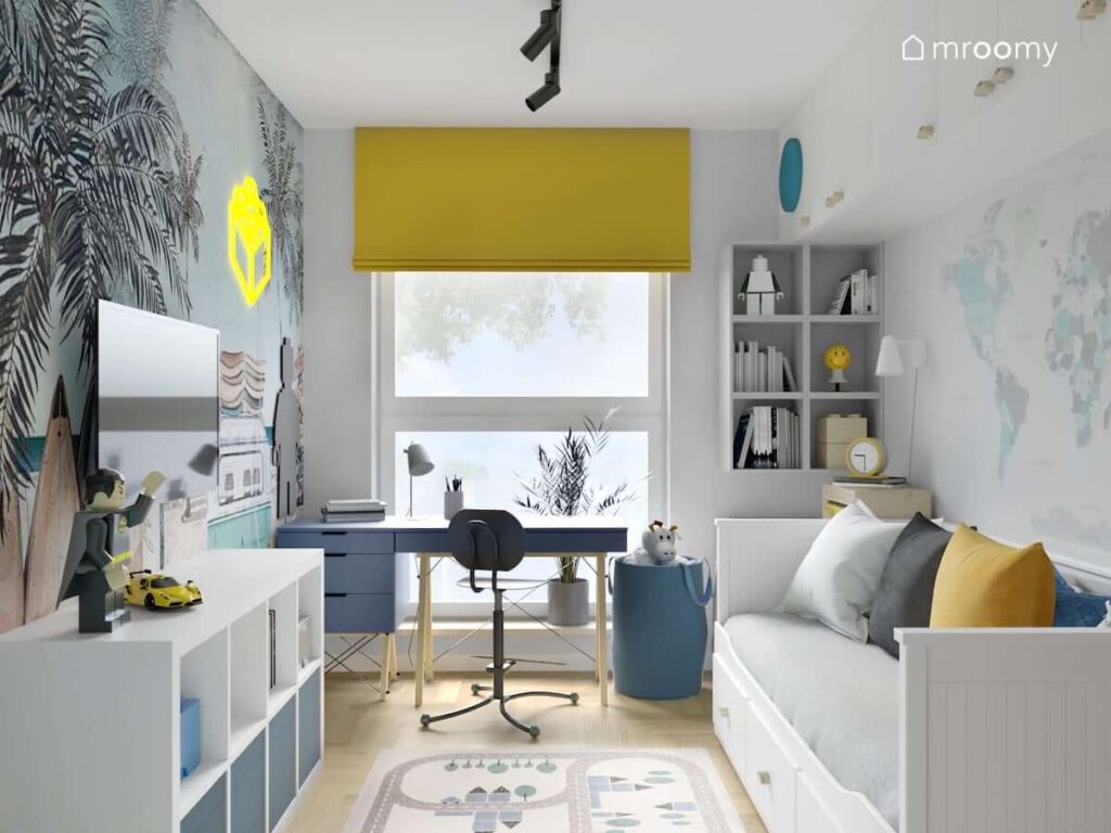 Jasny pokój dla chłopca z białym łóżkiem i regałami oraz granatowym biurkiem na drewnianych nogach niebieskim koszem na zabawki i żółtą roletą rzymską