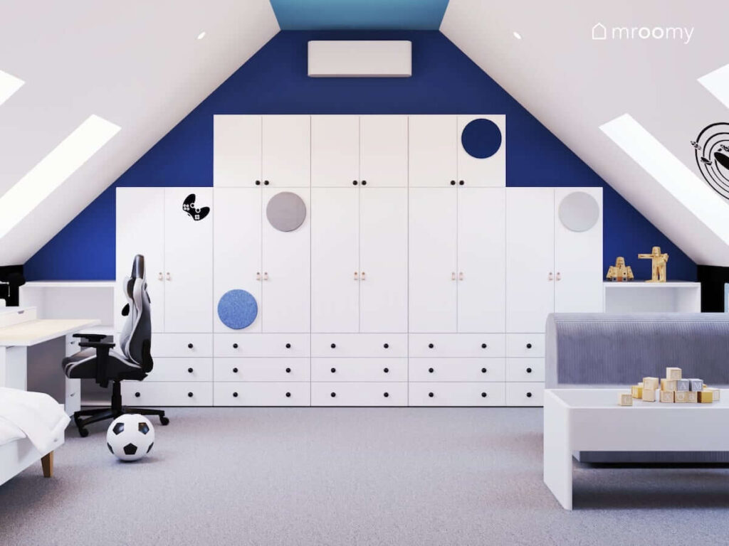 Biała szafa modułowa w pokoju dla chłopca uzupełniona miękkimi panelami i naklejką w kształcie pada