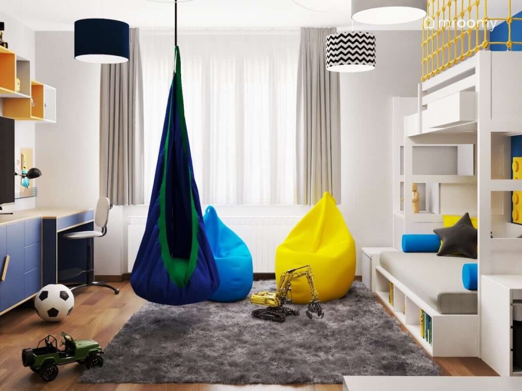 Jasny pokój dla chłopca w wieku szkolnym a w nim łóżko piętrowe niebieska i żółta pufa huśtawka kokon oraz szary futerkowy dywan