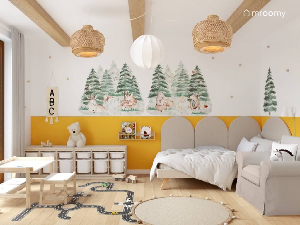 Biało żółty pokój dla chłopca ze ścianami ozdobionymi leśnymi motywami oraz z biało drewnianymi meblami i naklejką podłogową w kształcie jezdni