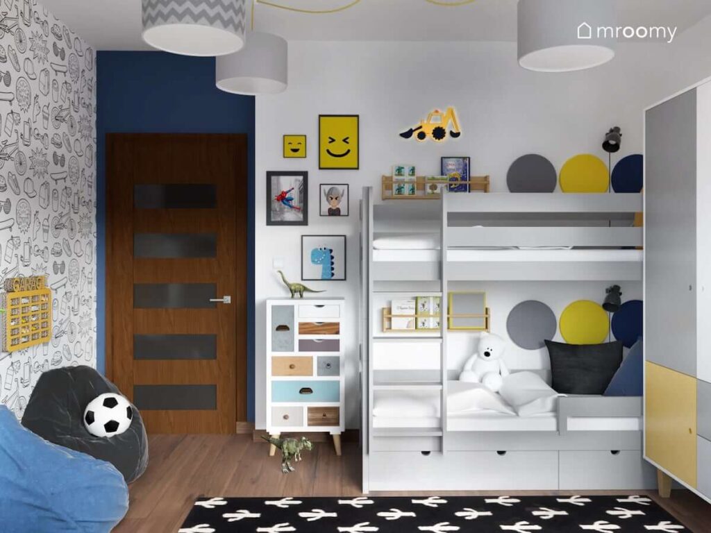 Szare łóżko piętrowe uzupełnione panelami ściennymi w różnych kolorach i drewnianymi szafkami a także ozdobne plakaty lampka w kształcie koparki oraz komoda z kolorowymi szufladami w pokoju dla dwóch braci