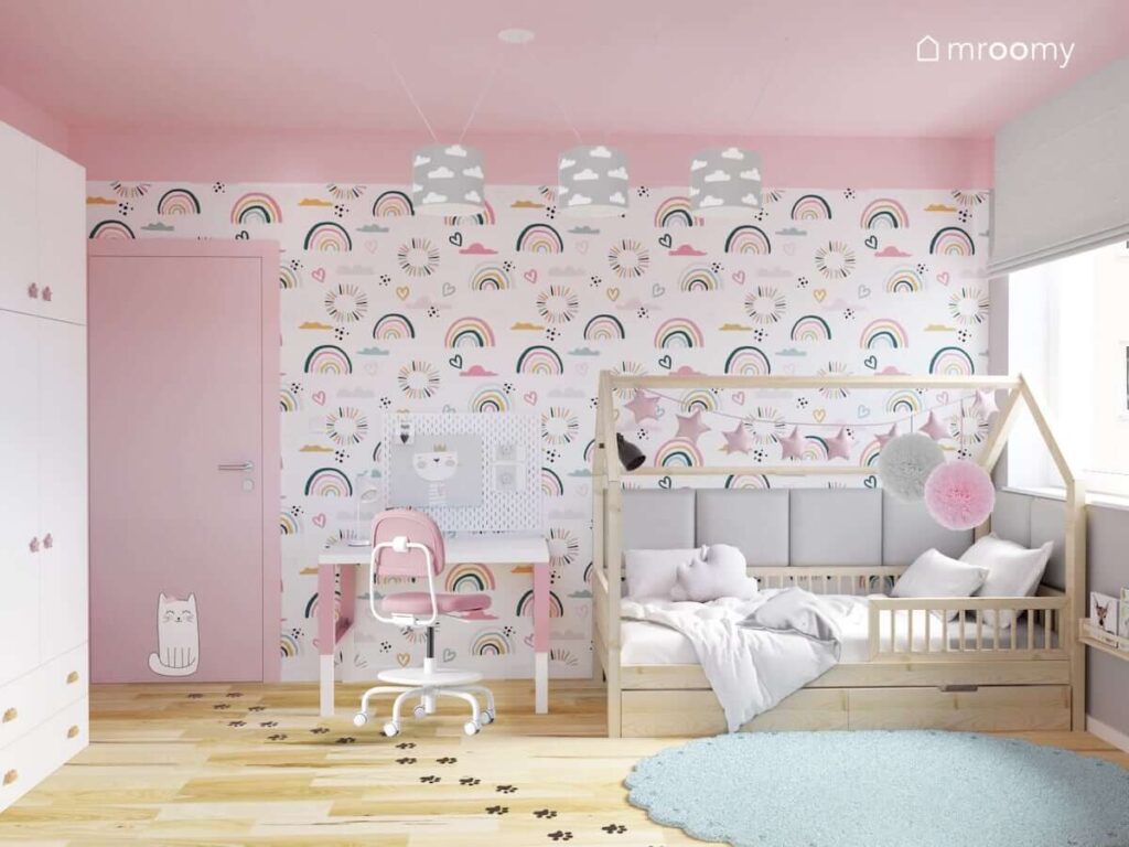 Różowo szary pokój dla dwóch dziewczynek z drewnianym łóżkiem domkiem biało różowym biurkiem z organizerem i ścianą pokrytą tapetą w tęcze