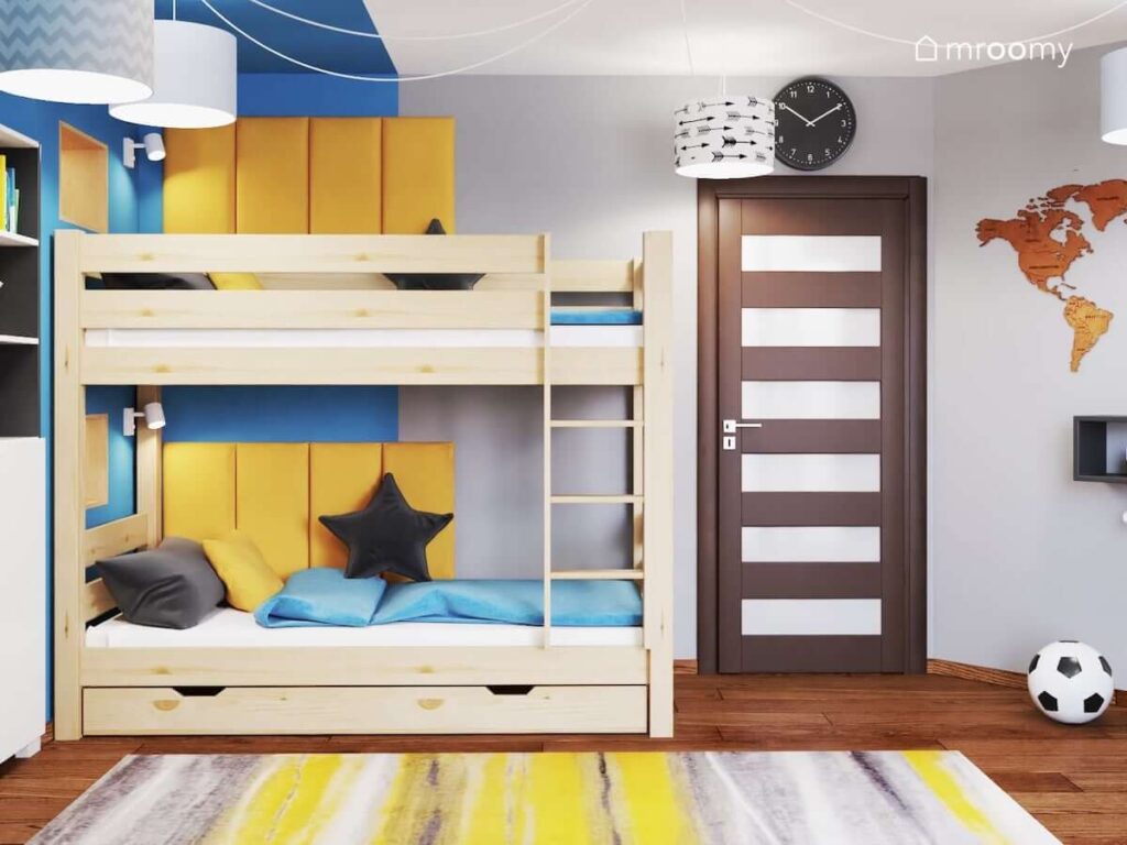 Drewniane łóżko piętrowe uzupełnione żółtymi panelami ściennymi a także żółto szary dywan i czarny zegar ścienny w pokoju dwóch chłopców w wieku szkolnym