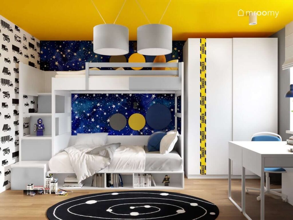 Łóżko piętrowe uzupełnione panelami ściennymi a za nim gwieździsta tapeta a obok biała szafa w barwnym pokoju dla dwóch chłopców