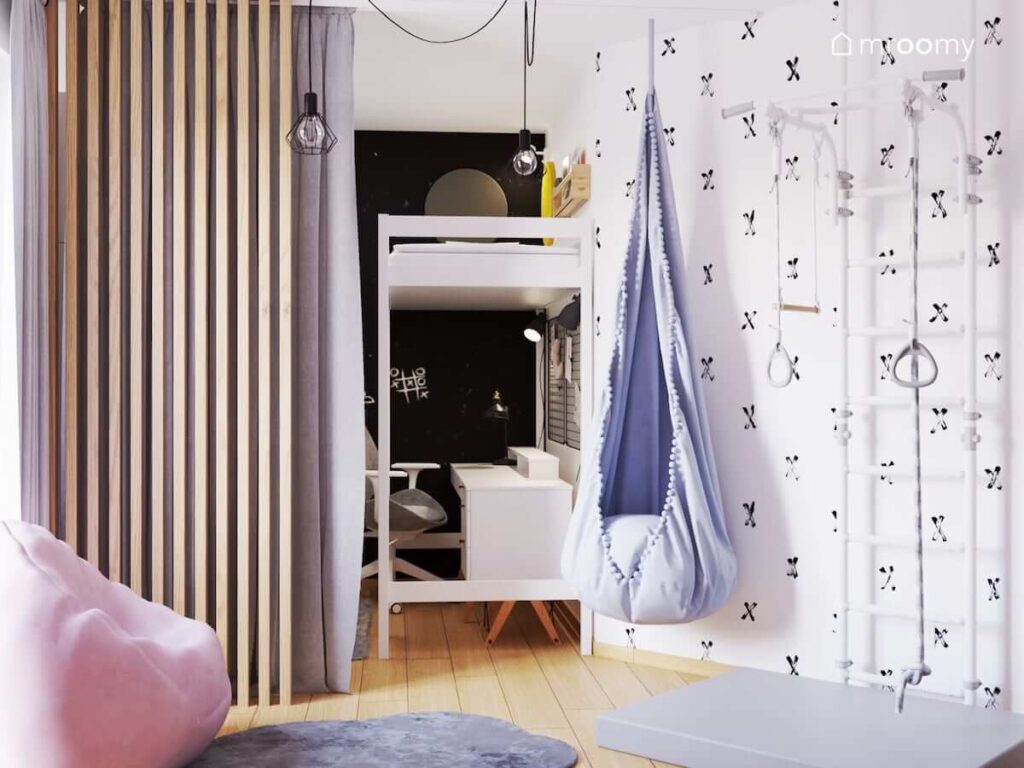 Biała drabinka gimnastyczna szara huśtawka kokon a za nimi ściana pokryta tapetą w iksy w pokoju dla dwóch dziewczynek