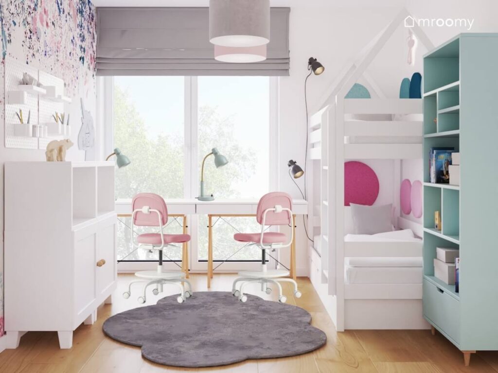 Łóżko piętrowe w kształcie domku oraz dwa biurka z różowymi krzesłami i szary dywanik w kształcie chmurki w pokoju dla dwóch sióstr