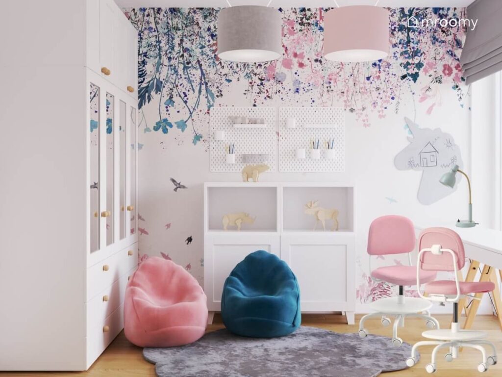Jasny pokój dla dziewczynek a w nim szafa z lustrzanymi drontami różowy i niebieski worek do siedzenia białe komody organizery ścienne i kwiecista tapeta