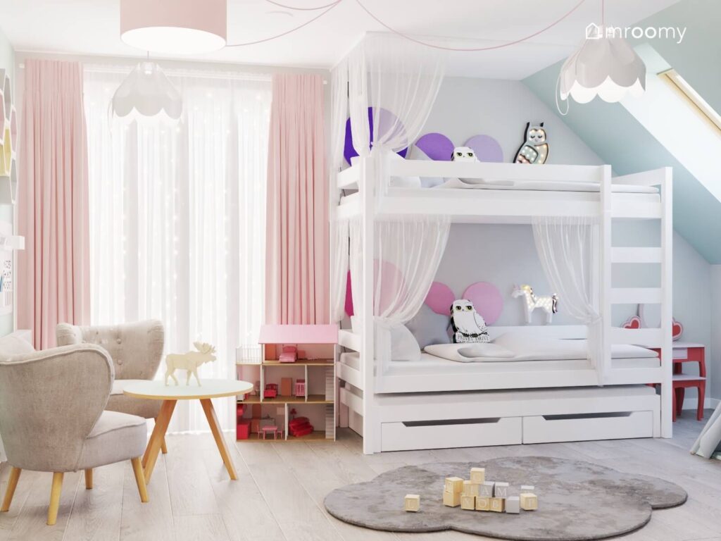 Kolorowy pokój dla dwóch dziewczynek ze stolikiem z dwoma fotelami oraz z białym łóżkiem piętrowym uzupełnionym firankami miękkimi panelami oraz dodatkami w kształcie sów