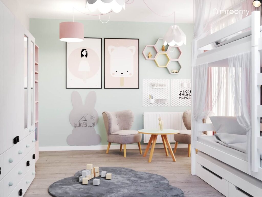 Biało miętowy pokój dla dwóch dziewczynek a w nim łóżko piętrowe stolik na drewnianych nogach z fotelami organizery ścienne ozdobne plakaty i tablica kredowa w kształcie królika