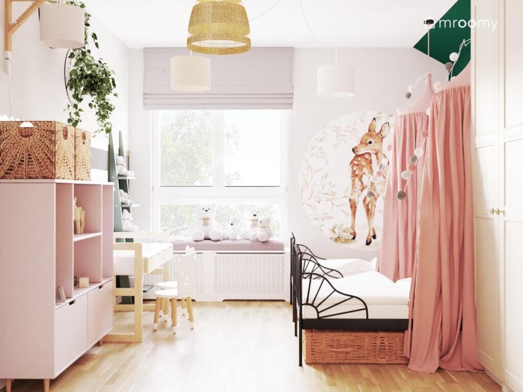Jasny pokój dla dwóch dziewczynek a w nim czarne łóżka różowy regał z szufladami oraz naklejka ścienna w kształcie sarenki