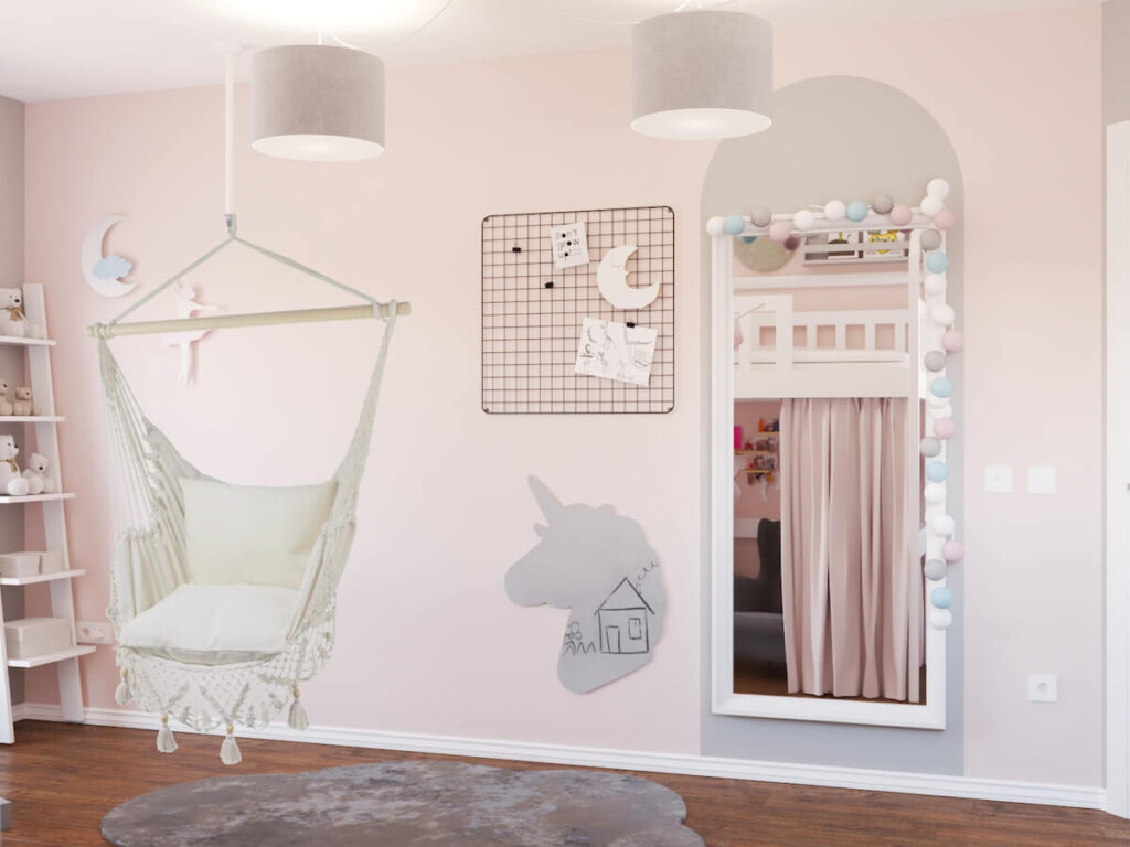 Ściana w pokoju dla kilkulatki z dużym lustrem ozdobionym girlandą cotton balls z organizerem ściennym oraz tablicą kredową w kształcie jednorożca a także wiszący fotel hamak