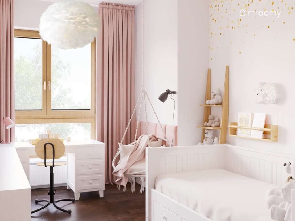 Jasny pokój dla kilkulatki z białymi meblami oraz różowymi dodatkami oraz z wiszącym fotelem hamakiem