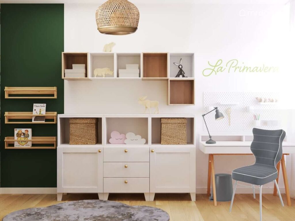 Drewniane półki ścienne oraz komoda a także białe biurko na drewnianych nogach w biało zielonym wiosennym pokoju dla dziewczynki