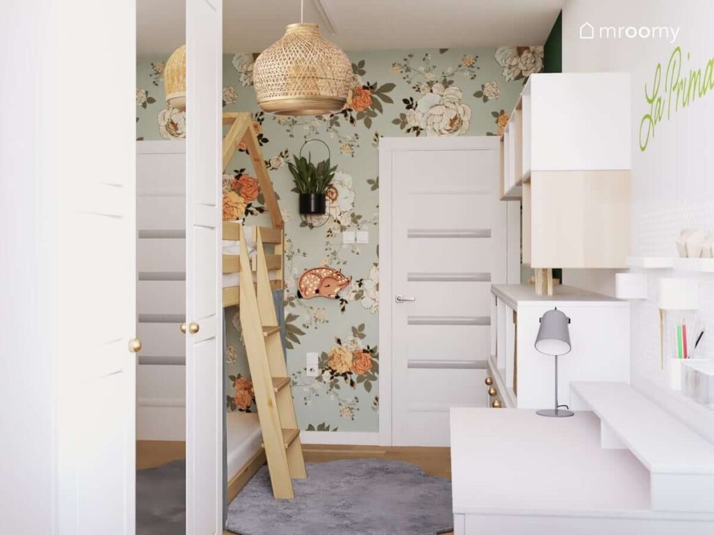 Wiosenny pokój dla dziewczynki z białymi szafkami i komodą drewnianym łóżkiem w kształcie domku bambusową lampą oraz ścianą ozdobioną kwiecistą tapetą