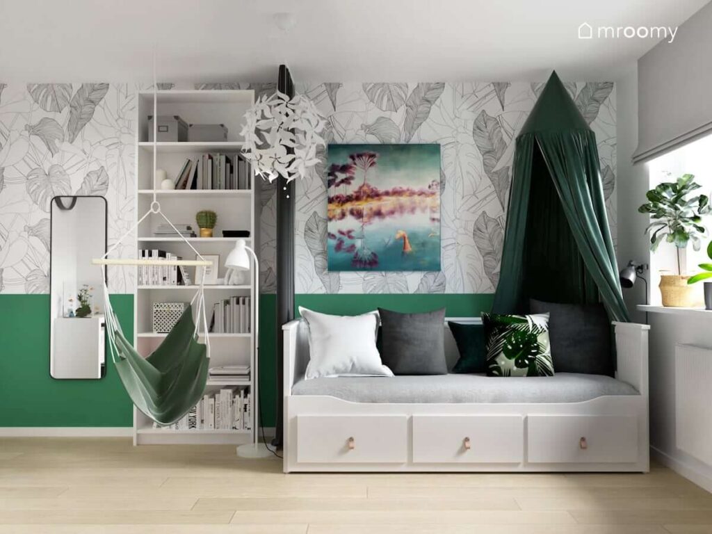 Strefa spania w pokoju dla nastolatki z łóżkiem z szufladami uzupełnionym zielonym baldachimem a za nim ściana pokryta tapetą w liście