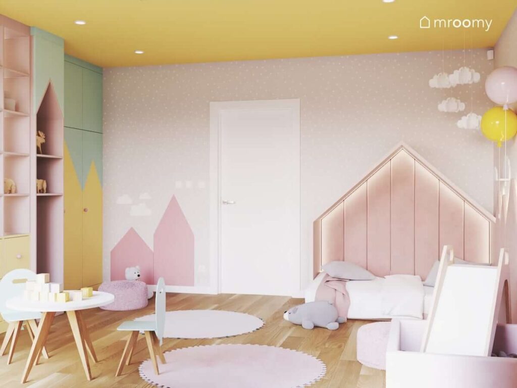Łóżko w kształcie trójkątnego domku a także ozdoby w kształcie chmurek w pastelowym pokoju dla małej dziewczynki