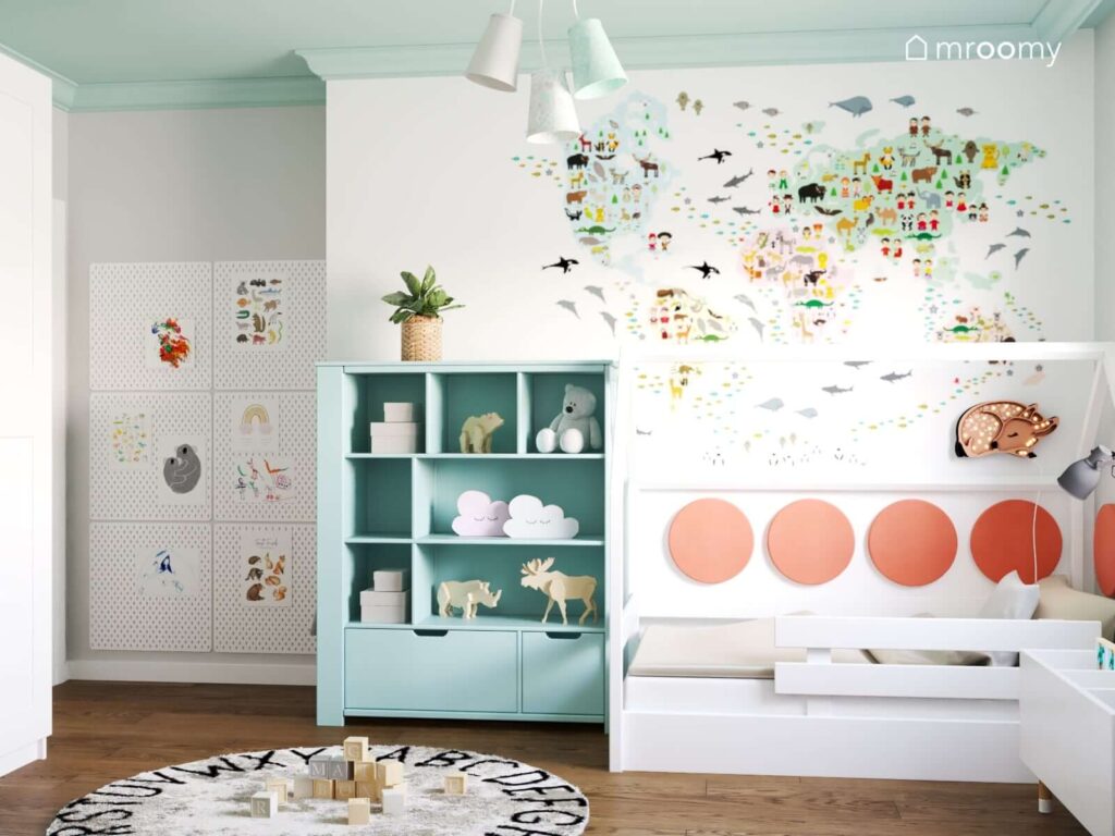 Biało miętowy pokój dla małej dziewczynki z miętowym regałem i białym łóżkiem domkiem uzupełnionym panelami ściennymi i lampką w kształcie sarenki a na ścianie kolorowa mapa świata i kilka organizerów