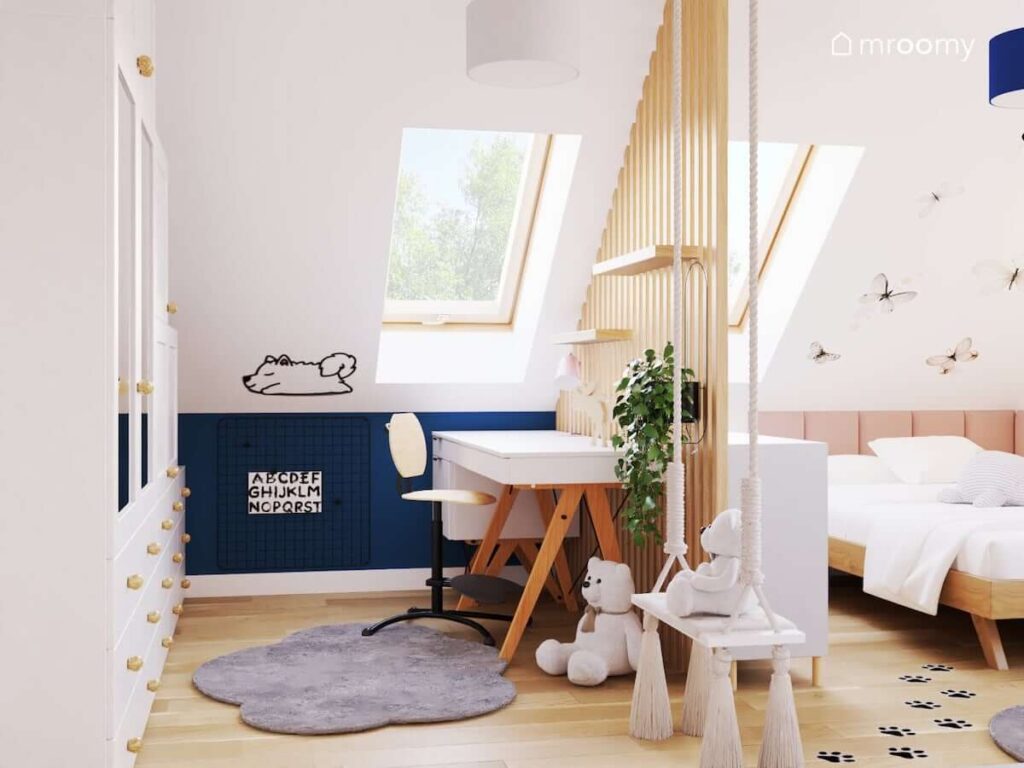 Biało niebieski poddaszowy pokój dla dziewczynki z białym biurkiem na drewnianych nogach huśtawką wiszącą drewnianą ścianką działową i naklejką w kształcie psa na skosie